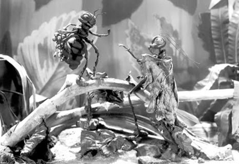 A black and white image shows 2 bug-like creatures standing towards one another in a natural environment with branches and leaves.