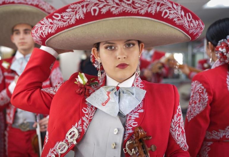 Woman in a red mariachi band uniform stands among others in similar dress