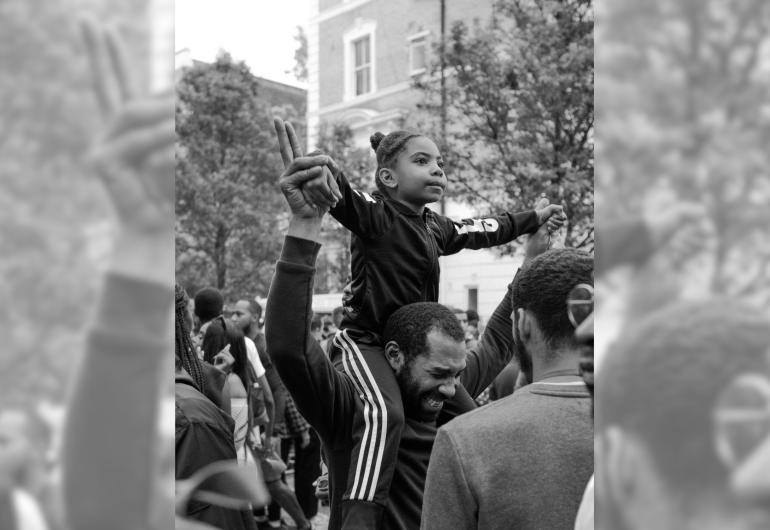 Black and white image of a young black girl on the shoulders of a man in a crowd