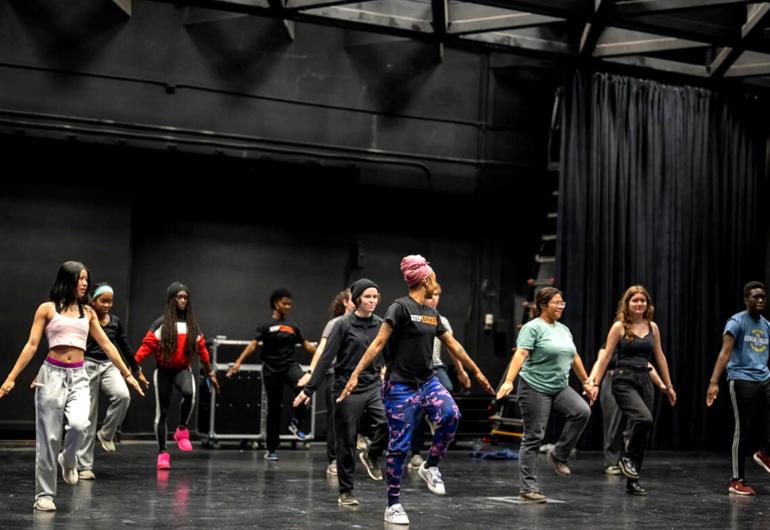 Step Afrika dancer leading others in a dance class on stage.