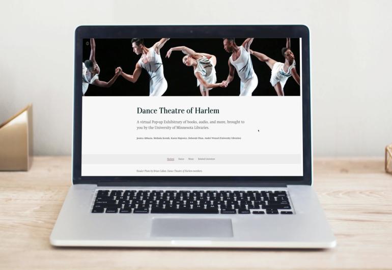 A computer screen on a desk that features an article about The Dance Theatre of Harlem. The article features a photo of the dancers in a white costume linking hands.