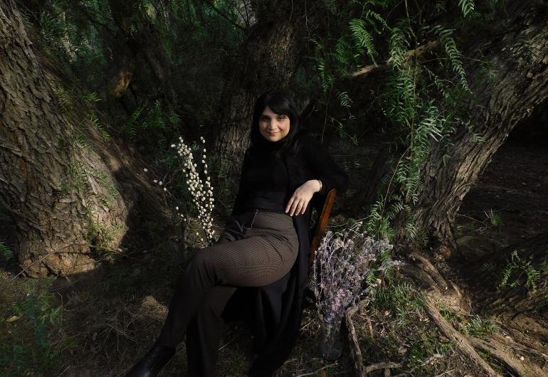 Sarah Davachi poses in front of two tree trunks