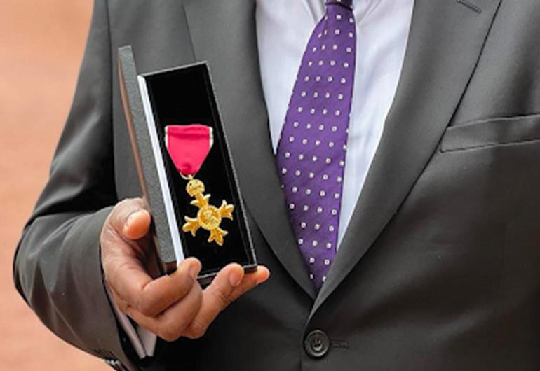 Close up of a hand holding a gold cross medal with a red ribbon in a small box