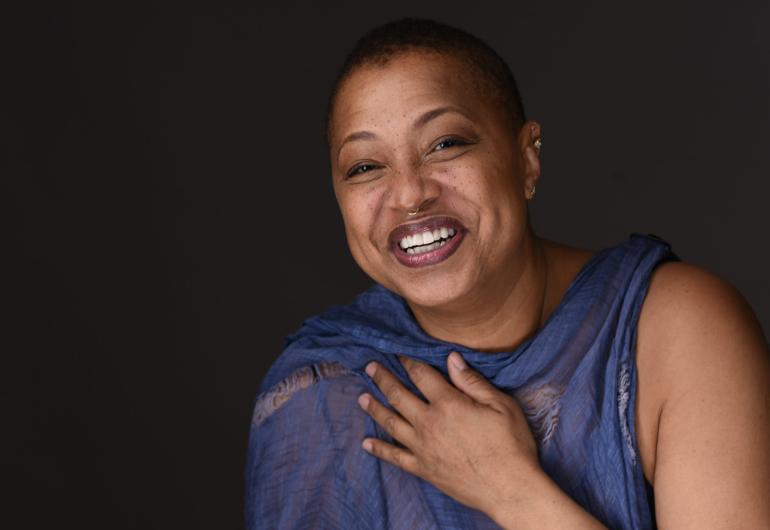 Lisa Fischer smiling in front of a dark gray background, looking into the camera. 