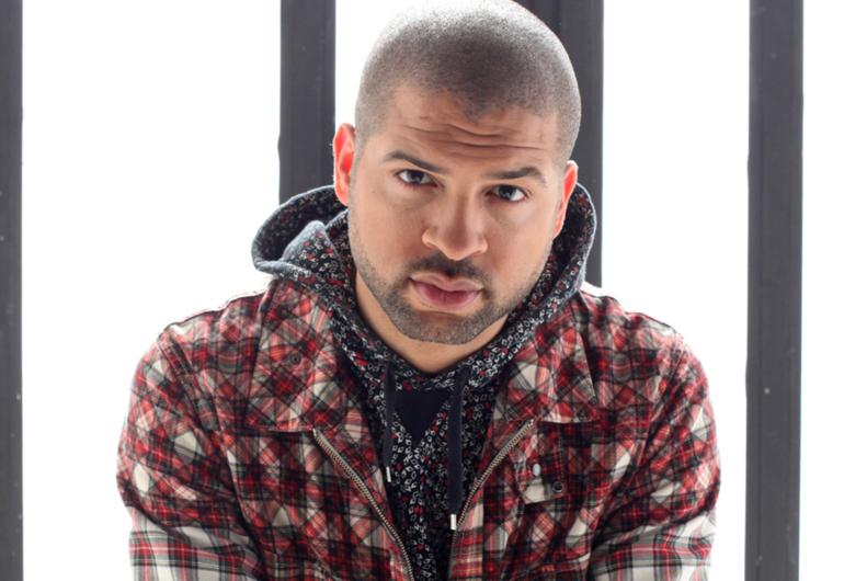 Jason Moran in front of a white and gray background, looking into the camera. 