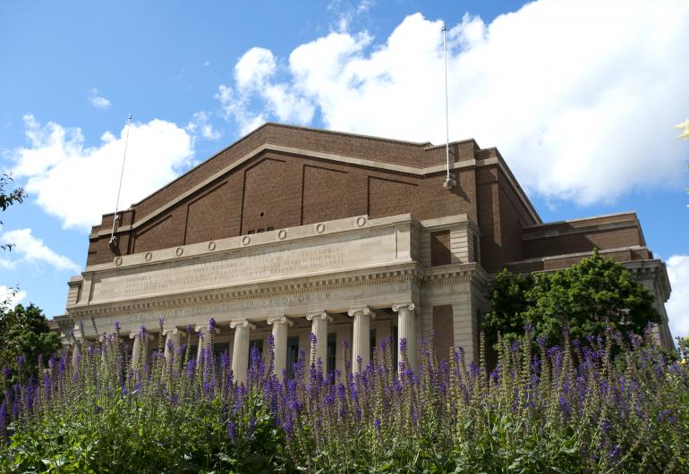 Northrop exterior under a blue sky with fluffy clouds and purple flowers in the foreground