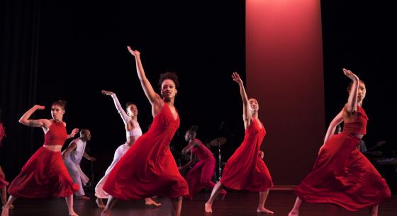 Group of dancers in red one arm raised, legs wide apart