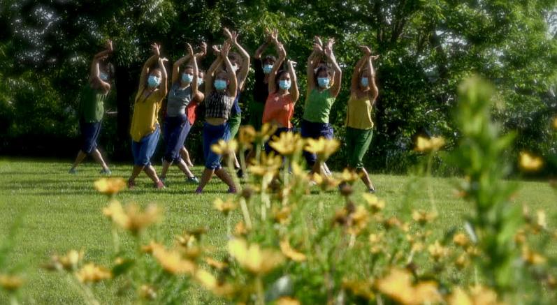 Dancers perform outside on a lawn with flowers in the foreground.