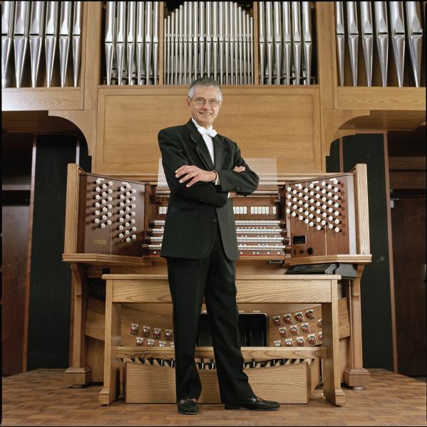 Olivera standing in front of the organ with his arms crossed
