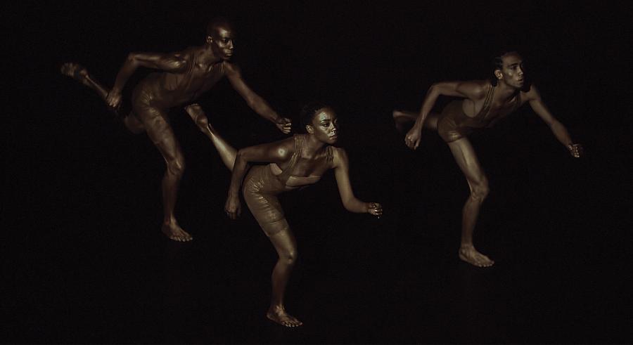 Three dancers appear in dark lighting, each holding a running position and looking to the right. 