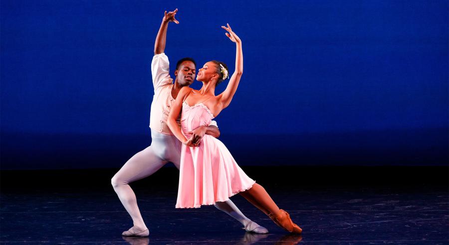 Male dancer in white lunging and holding the waist of female dancer in pink in deep lean forward. 
