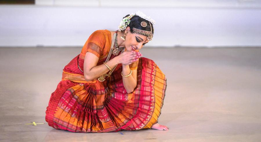Dancer in bright colors crouches with hands clasped.