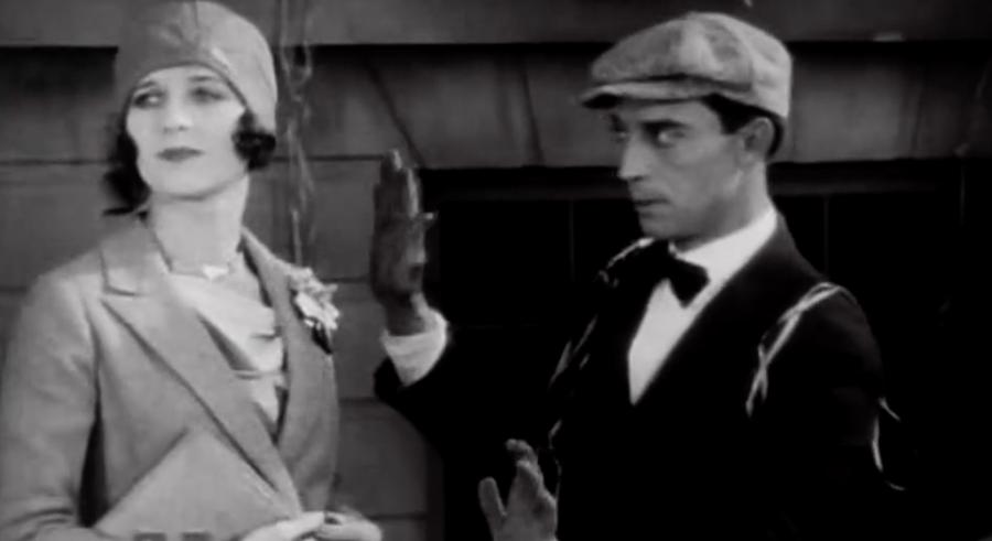 Buster Keaton raises a gloved hand in front of Marceline Day, in a still from The Cameraman.