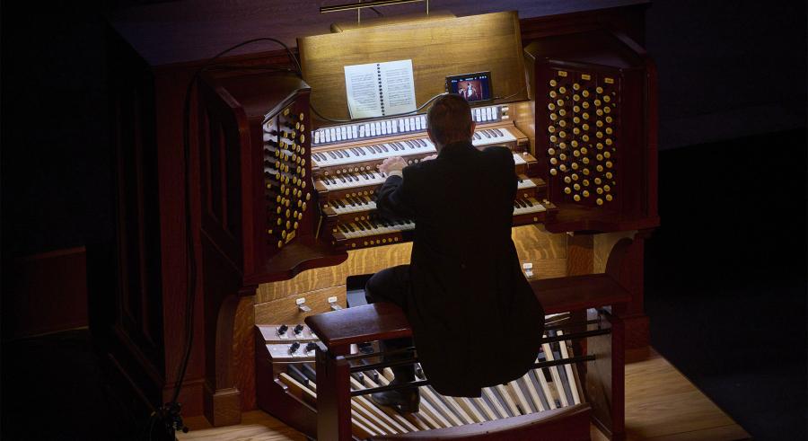 Back profile of Aaron David Miller playing organ in a dark theater