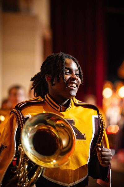 Musician in UMN Marching Band uniform smiles at something out of frame