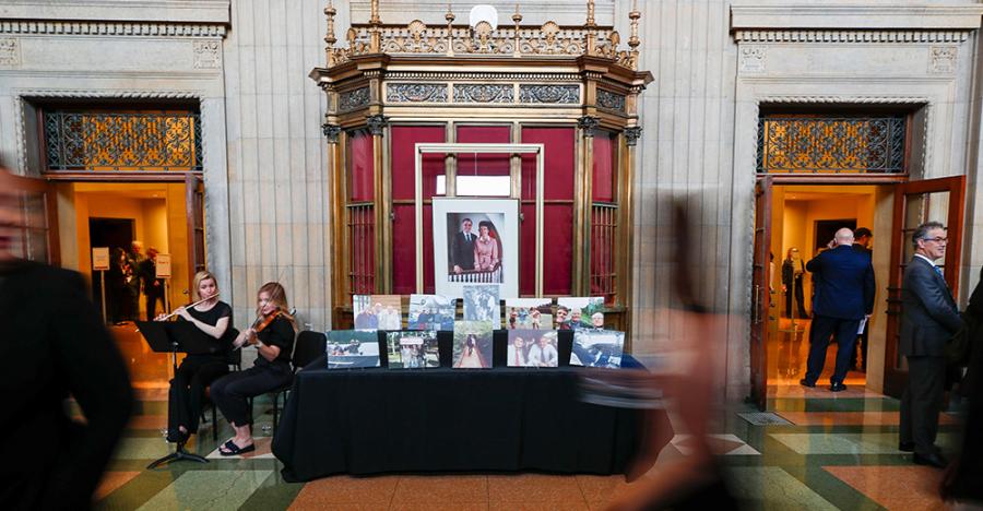 The Northrop Atrium and an old ticket booth filled with photos of Walter Mondale. There is one larger image on the ticket booth and a table with two rows of images of Walter Mondale and his family and friends. A violinist and flutist play while patrons pay their respects. 