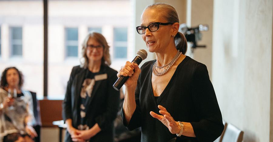 Artistic Director of Martha Graham Dance Company, Janet Eilber delivers a speech. Eilber is in a black dress with pearls on her neck and black glasses.