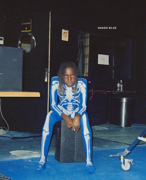 A person in a blue skeleton costume sits and stares into the camera