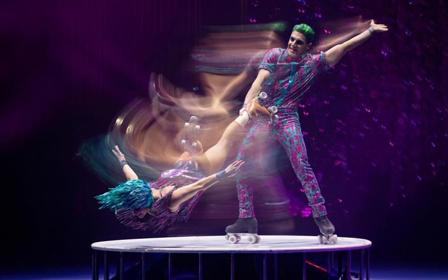 Motion image of a couple on roller skates. He is holder her by the ankle as she is stretch above the floor flying through the air.
