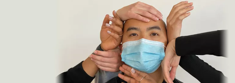 Dancing Our Way Out still - closeup of a person in a face mask surrounded by hands 