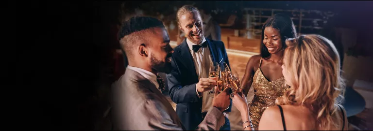 A group of people in cocktail attire smile and cheers with champaign glasses
