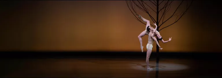 Male dancer in white shorts lifts female dance over his shoulder. Arms and legs bent at ninety-degrees.