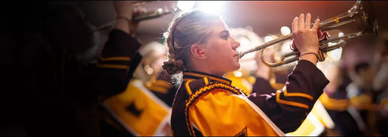 Trumpet player wearing a gold UMN Marching Band uniform.