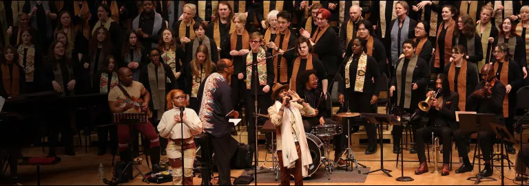 Two soloists at mics with the VocalEssence chorus behind them on risers.