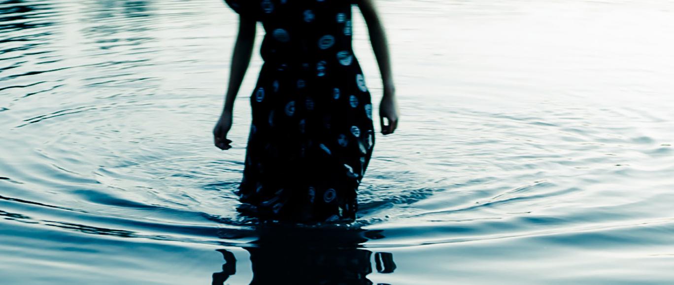 A woman wades into water in a floral dress
