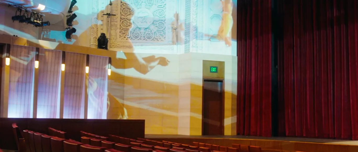 An empty theater with a projection of a dance performance on the walls.