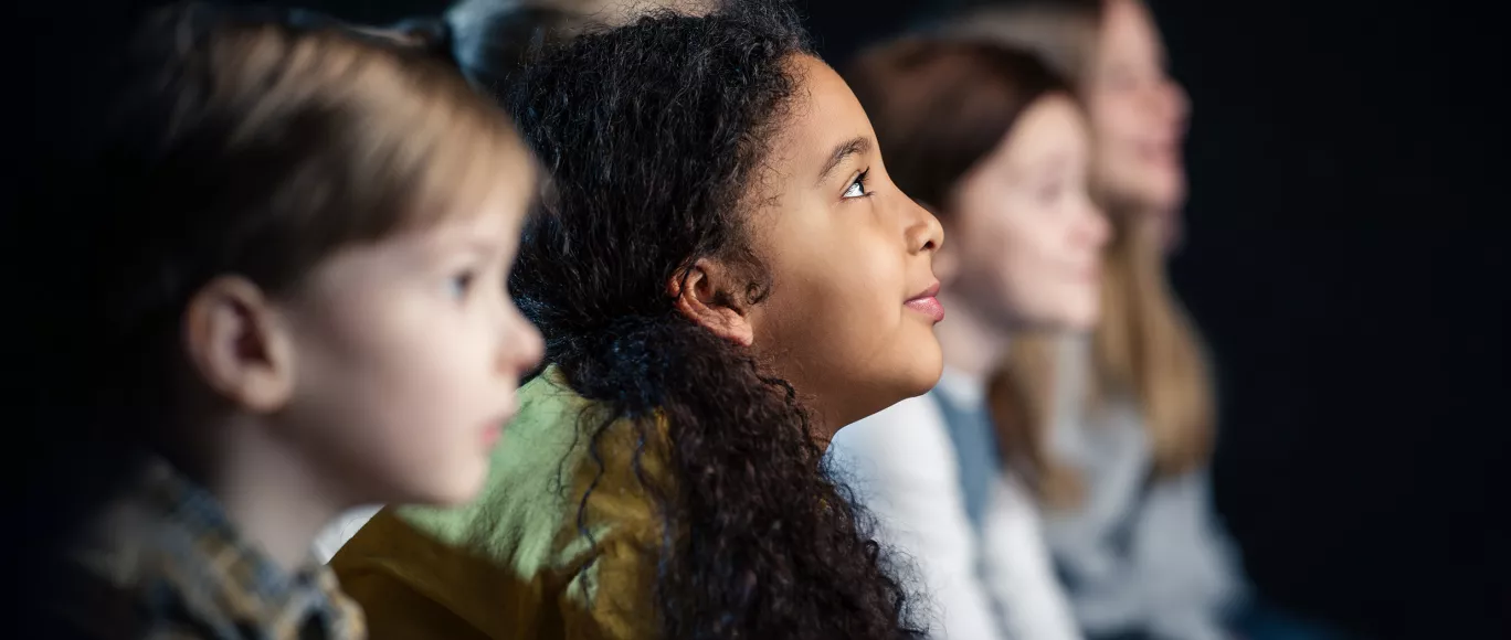 The side profiles of four children of varying races are shown as they are intently viewing something in front of them.