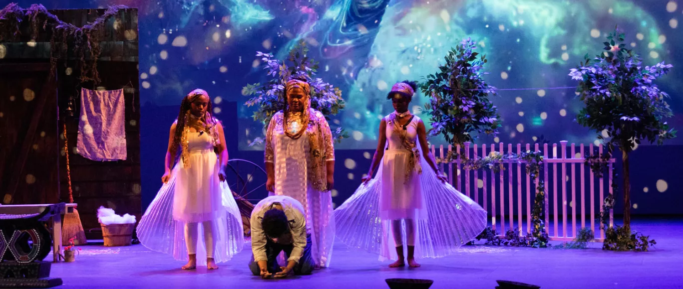 Three female performers in angelic costumes behind a male performer on his knees. An ethereal background projected in the background.