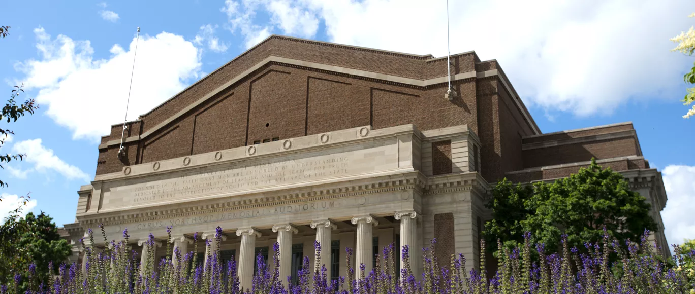 Northrop exterior under a blue sky with fluffy clouds and purple flowers in the foreground