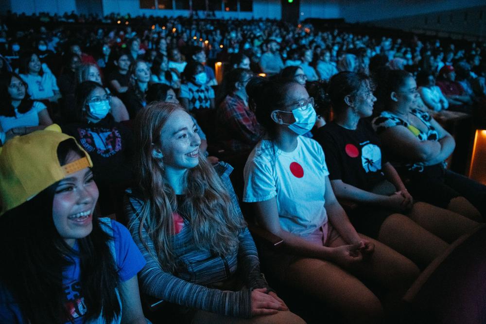 Students smile while watching a performance on stage