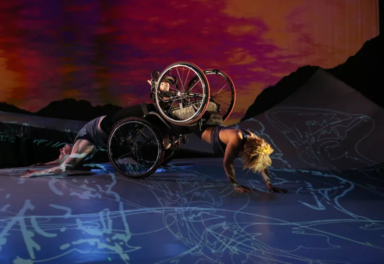 Alice Sheppard, a light-skinned Black woman with a crown of short curly hair, is crawling on her hands with her knees in Laurel Lawson's footplate. Laurel, a white woman, is arching her back on the ground as she is dragged along the floor. A sunset appears behind them.