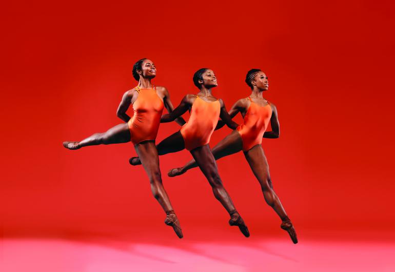 Three woman dancers from DTH in orange leotards leaping through the air in unison 