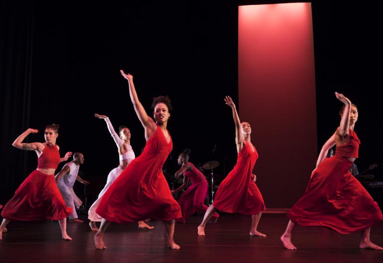 Group of dancers in red one arm raised, legs wide apart