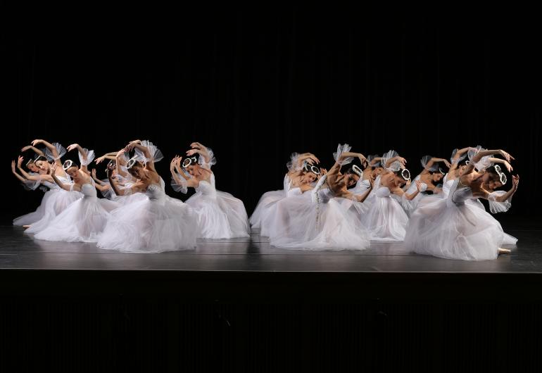Front view of the corps de ballet in bright white, on one knee leaning to the side with arms circling their heads