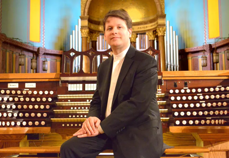 Sitting with his back to the keys of the organ, a bright aqua light on the walls behind
