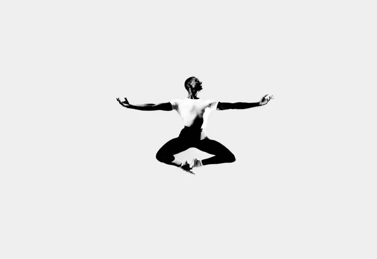 Arthur Mitchell jumps with knees bent, toes touching and arms out to the sides.