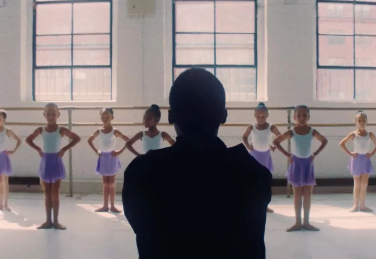 Children in ballet class standing in first position with their hands on their hips.