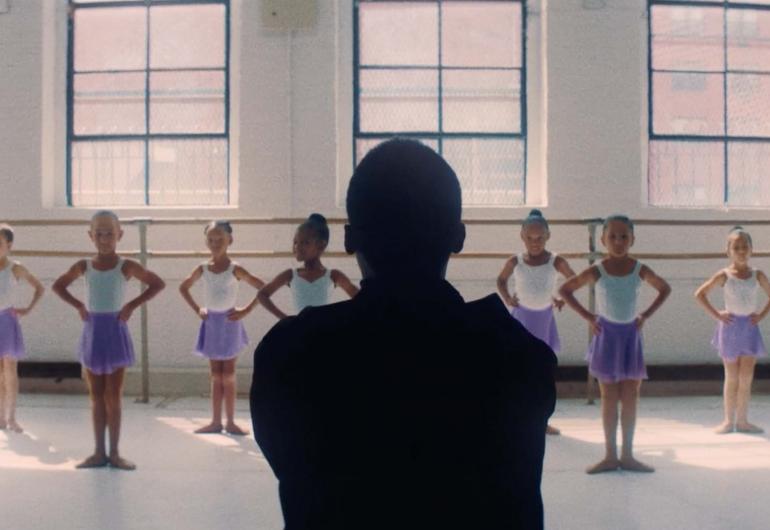 Children in ballet class standing in first position with their hands on their hips.