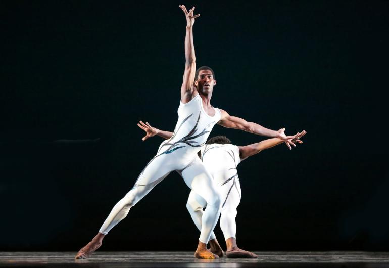 Dance Theatre of Harlem dancers wearing white perform on stage with a black background.