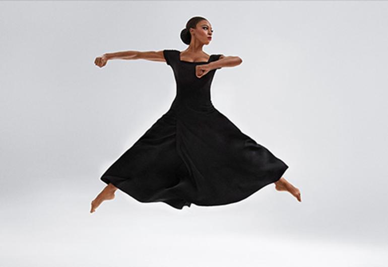 Leslie Andrea Williams in Martha Graham’s Chronicle - long black dress jumping with legs out to the sides and strong arms looking to the side