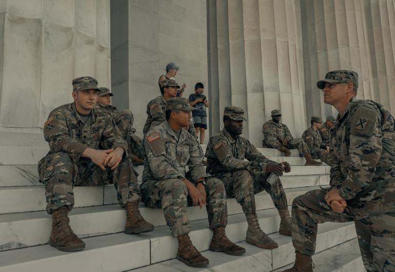 Military soldiers in fatigues sit on the steps of a building with columns