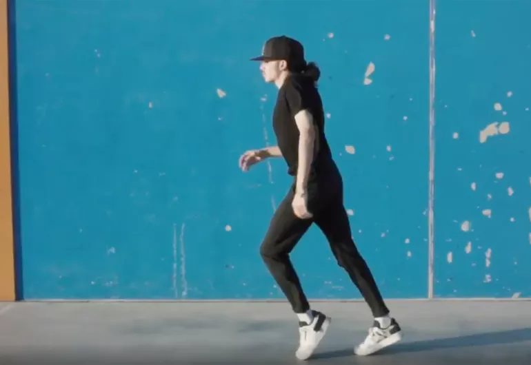 Video still of Cameron Murphy 'Moonwalking' on a sidewalk next to a teal wall.