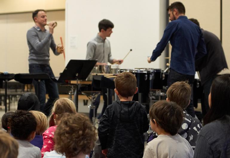 Musicians playing various percussion instruments in front of young children.