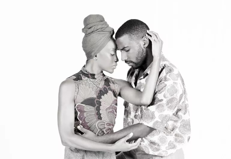 A man and woman touch foreheads, her arm touches his head, his arm around her waist