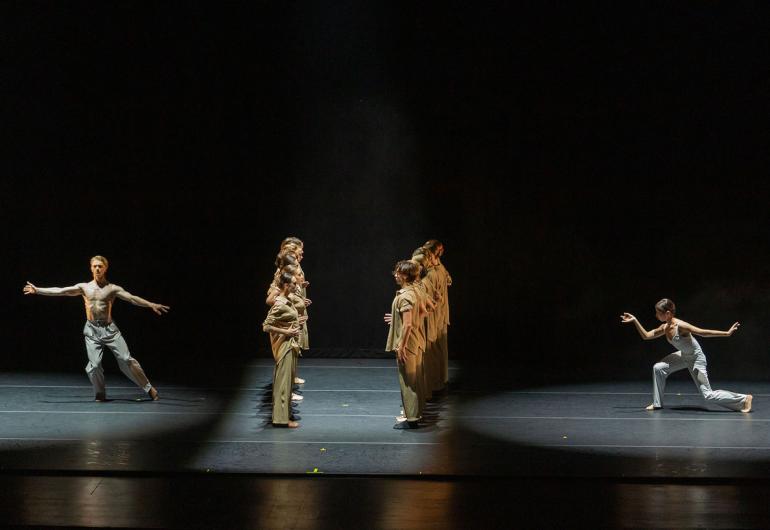 Two groups of dancers in lines facing eachother, one solo dancer posed behind each line