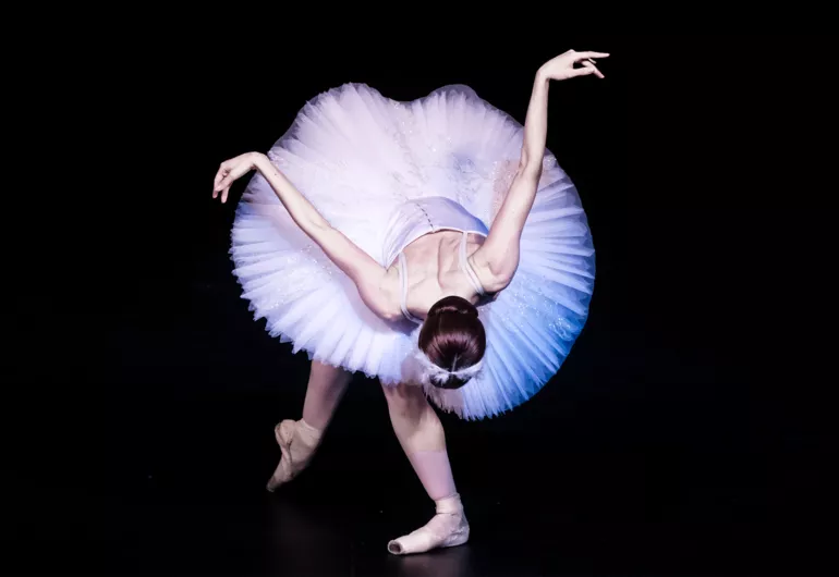 Ballerina in pink bows deeply forward, one toe pointed back and arms up behind her